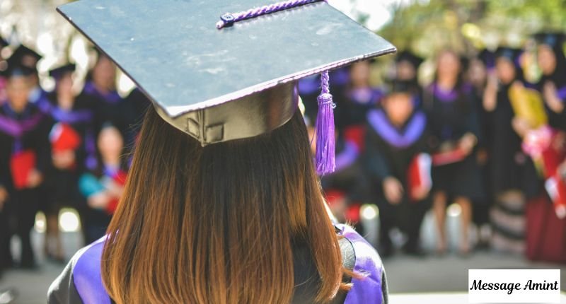 A female graduate wearing a black cap with a purple tassel, looking at a blurred crowd of graduates.